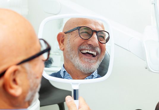 Man with black glasses smiling in reflection in mirror