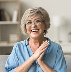 Senior woman with glasses smiling on couch at home