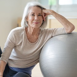 Senior woman smiling while resting against balance ball