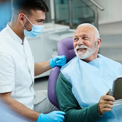 Senior patient looking at dentist while holding small mirror