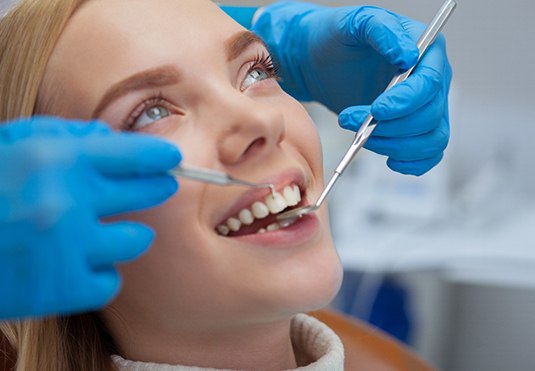 A dentist checking a smiling blonde woman’s teeth