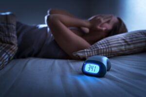 Sleepless person with alarm clock in foreground.