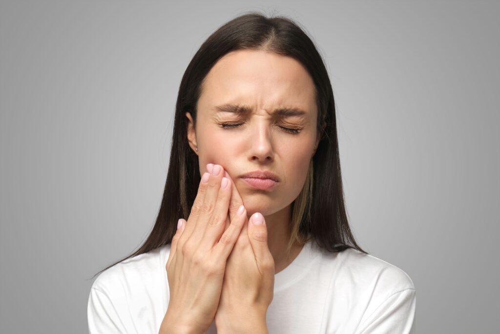 Woman with long dark hair pressing her fingers to her jawbone with eyes closed in pain