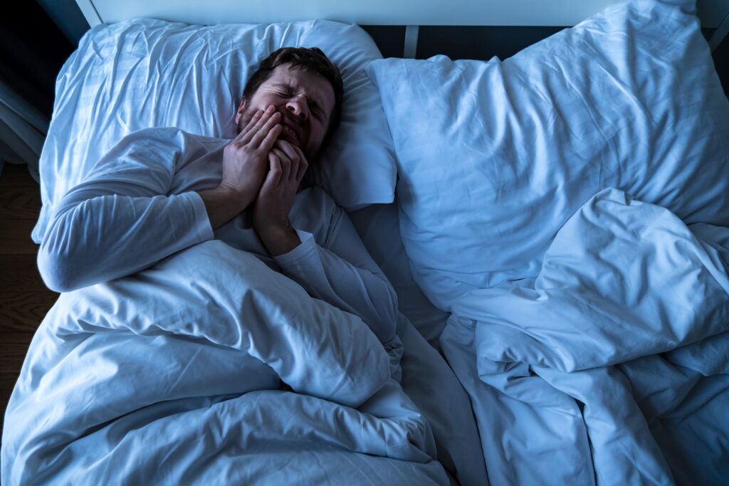 Man in bed holding hands to jaw in pain